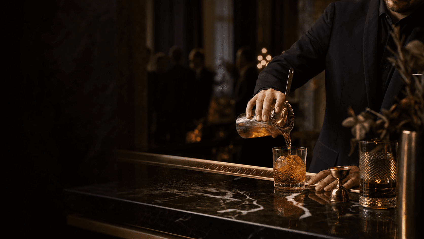 Mixologist pouring an amber cocktail at a black marble event bar